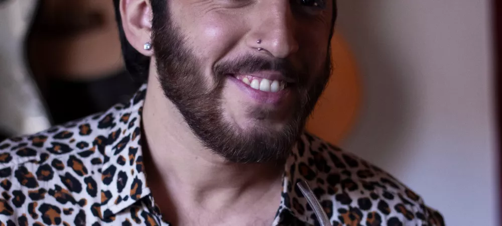 Image of the artist wearing an animal print shirt and smiling with a mate in his hand